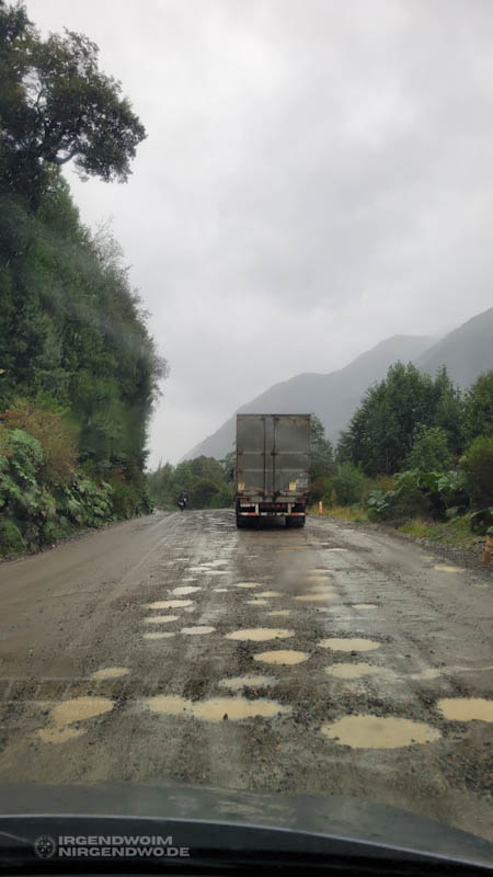 Mit braunem Wasser gefüllte Schlaglöcher und ein LKW auf der Carretera Austral / Ruta 7 in Chile
