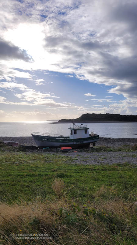 Kleines Boot an Land, dahinter Meer, eine Insel und Sonnenuntergang
